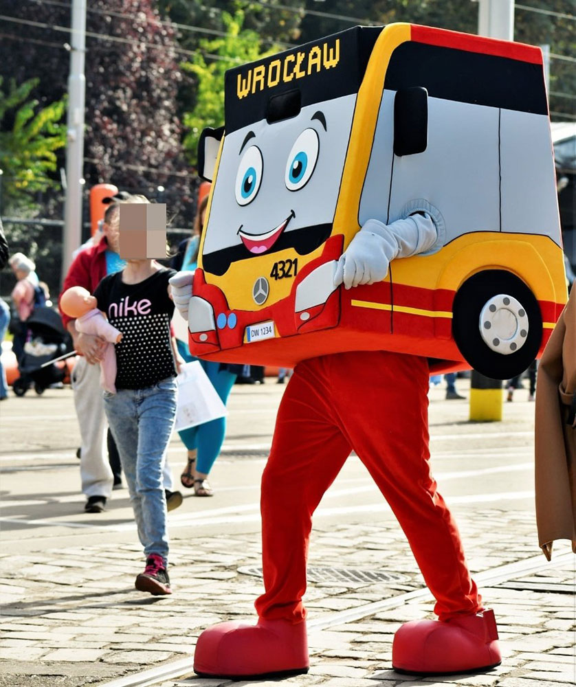 Na fotografii widnieje strój reklamowy w postaci autobusu na jednej z wrocławskich ulic. W tle przechodnie, jezdnie, słupy tramwajowe
